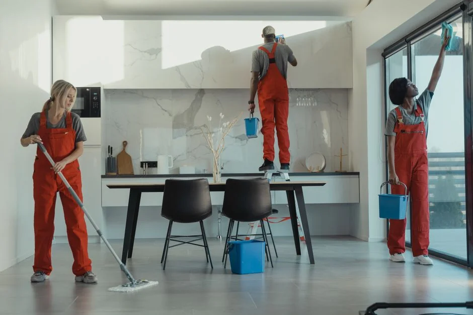 A professional cleaner in protective gear vacuuming the floor in a modern living room.